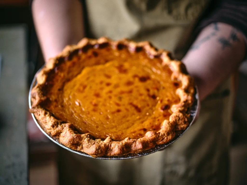 A person holds a freshly baked pumpkin pie with a golden-brown crust, ready to be served.