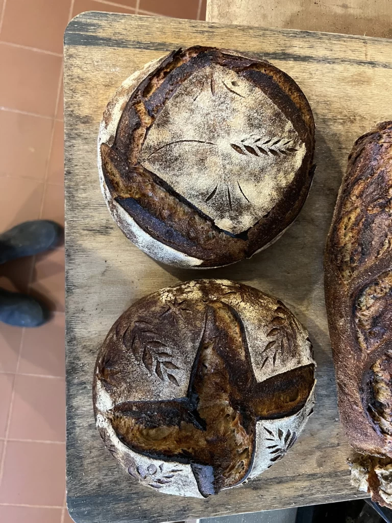 Three artisanal sourdough loaves with intricate scored designs on a wooden surface.