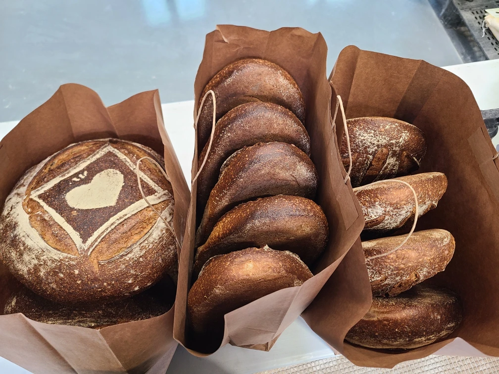 Two bags of artisanal bread: one round loaf with a heart design, and several round buns arranged neatly.